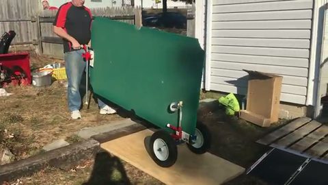 man wheeling a large slate panel on a dolly through a backyard, face visible