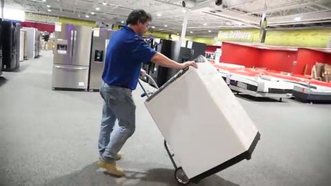 mover wheeling a white top-load washer on an appliance hand truck, face visible