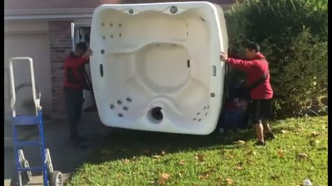 two movers carrying a hot tub across a yard, face visible