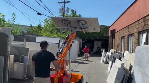 worker transporting a marble slab overhead on a powered lifter